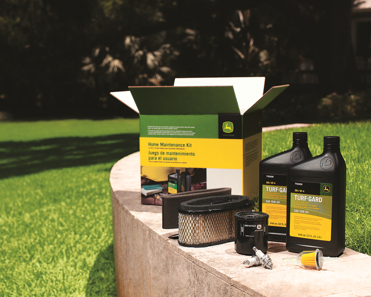 John Deere maintenance kit with oil, filters, and spark plugs on a ledge outdoors.
