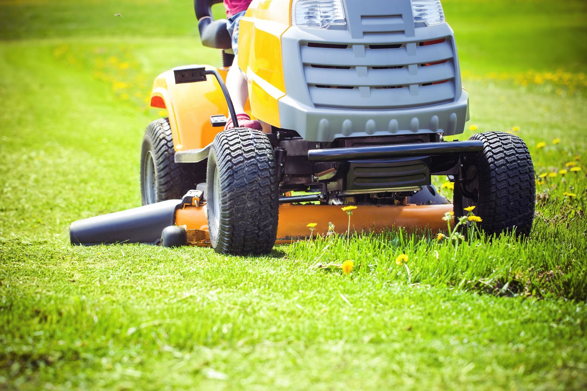 Yellow riding lawnmower mowing a green lawn with the operator visible.