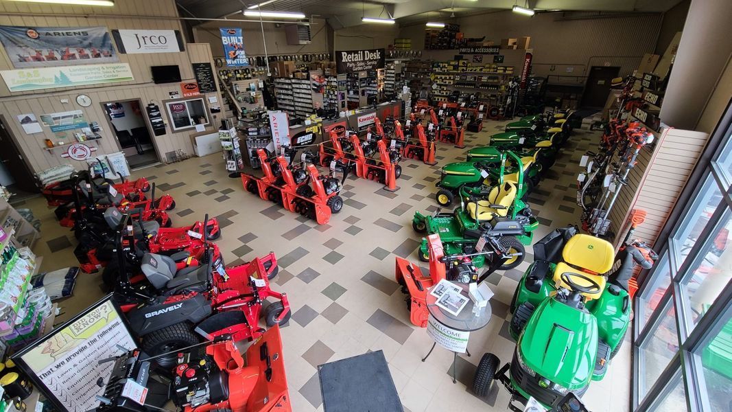 Inside a hardware store: snowblowers and lawn mowers on display. Red and green machinery on a tiled floor.