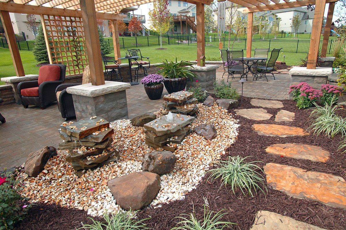A stone water feature sits amidst gravel in a landscaped patio