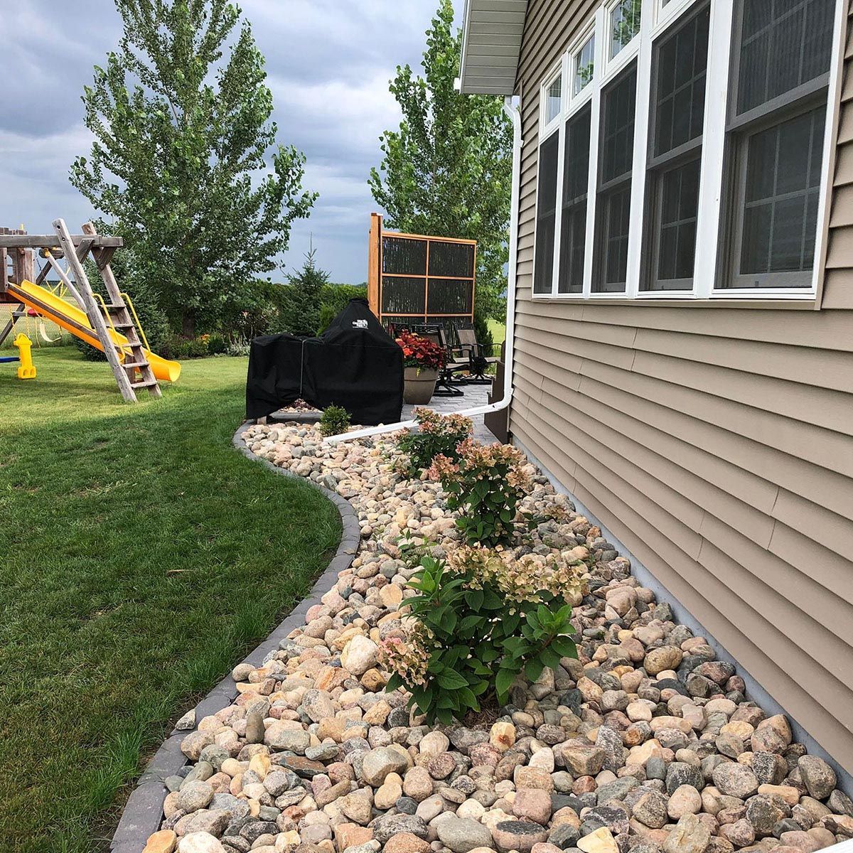 A tan-sided house with rock landscaping beds