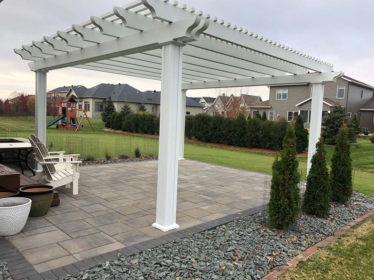 A white pergola stands over a stone patio in a backyard
