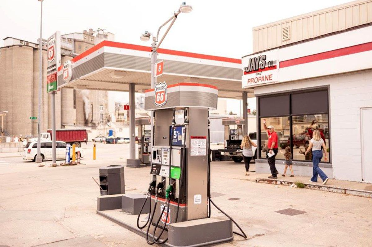 Gas station exterior with fuel pumps, red and gray canopy, people near building.