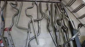 Metal exhaust pipes of various shapes and sizes, leaning against a wall.