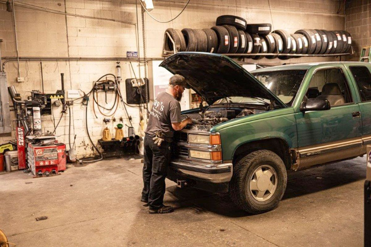 Mechanic working on a green SUV in a garage. Hood is up. Tires on a shelf.