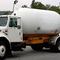 White propane tanker truck, yellow frame, parked on a road.