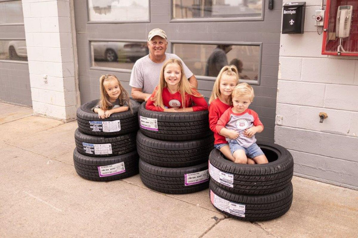 A man and four children pose in tires stacked in front of a garage.