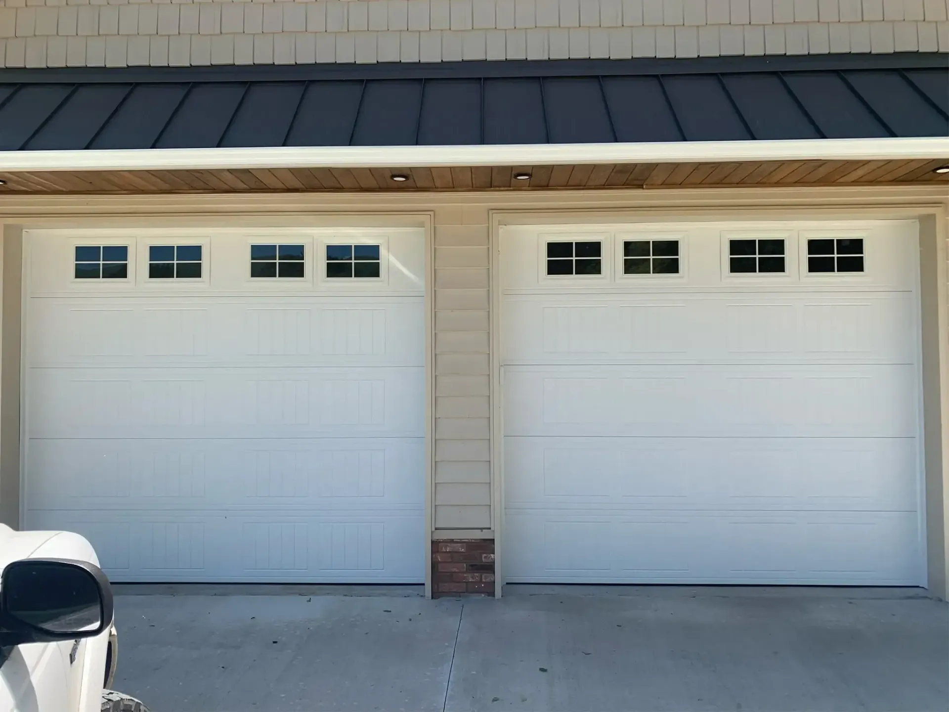 Two white garage doors on a beige house with a black-trimmed roofline