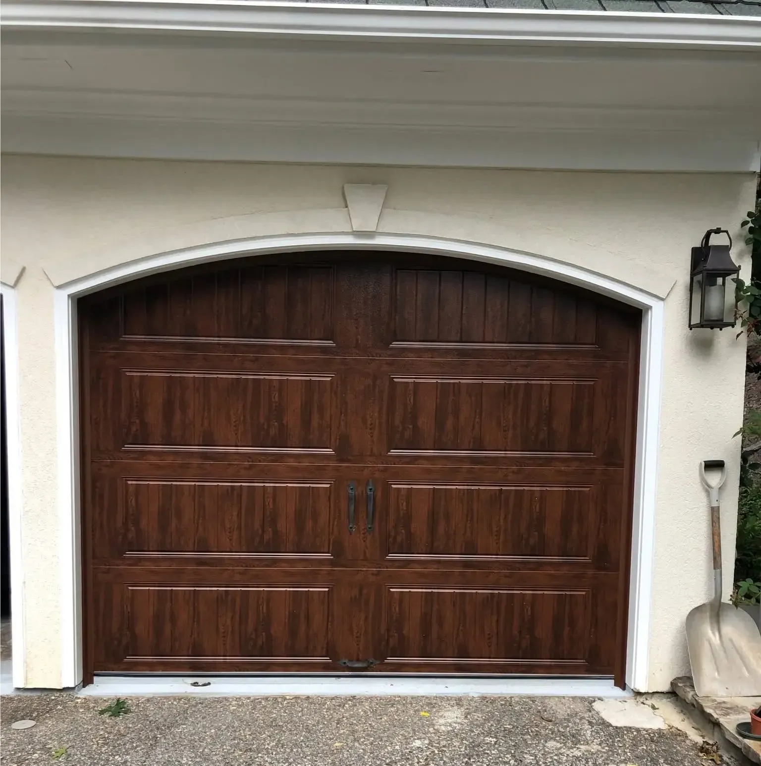Wooden arched double garage door beneath a white stucco exterior with a lantern light on the right.
