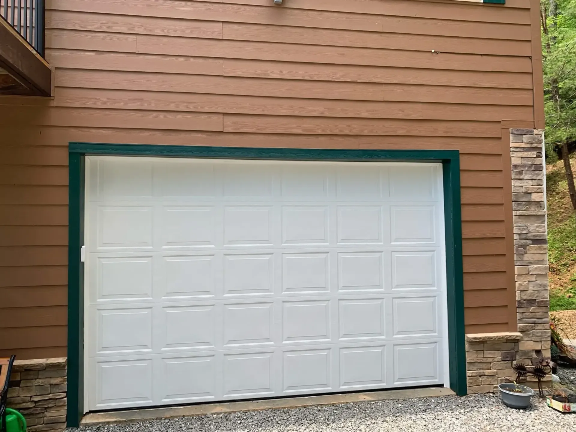 White garage door framed by teal trim on a brown house exterior