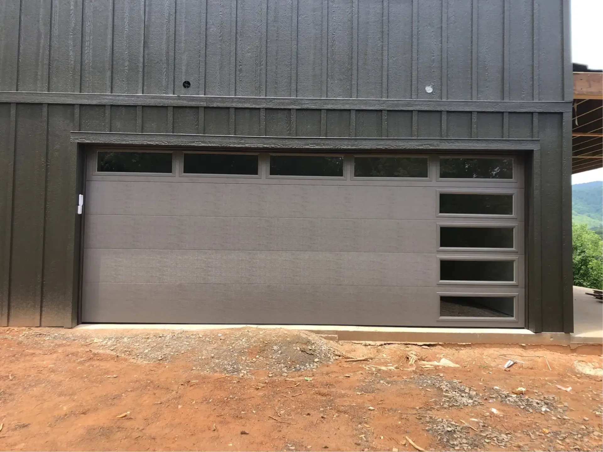 Gray garage door set into a dark wooden building above a dirt driveway.