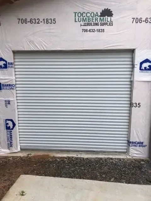 Gray roll-up garage door on a building under construction, with house wrap and gravel foreground