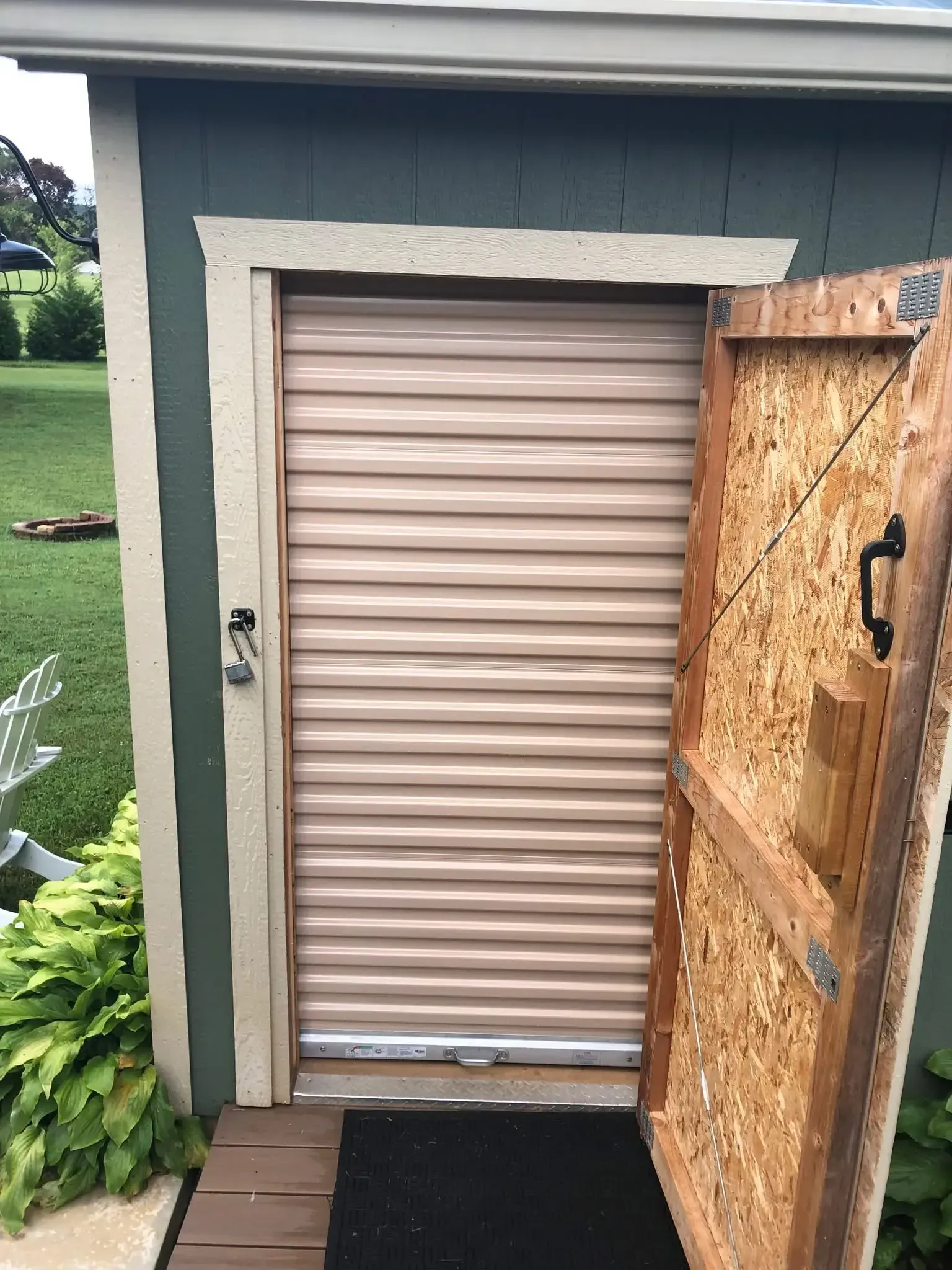 Closed beige roll-up shed door beside an open wooden gate in a small yard.