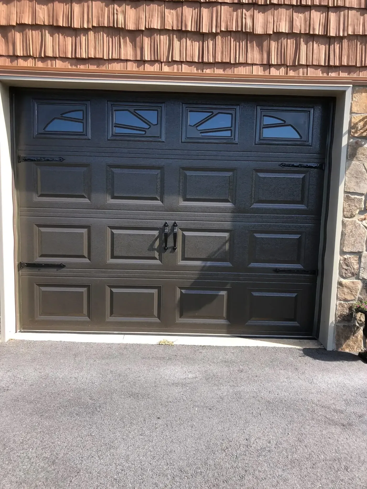 Black garage door with four small windows at the top, set in a stone house exterior.