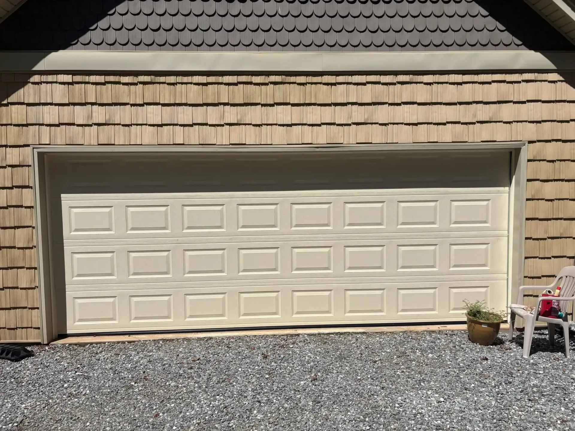 Two-car garage with cream door and tan siding, gravel driveway, and small plants by the entrance