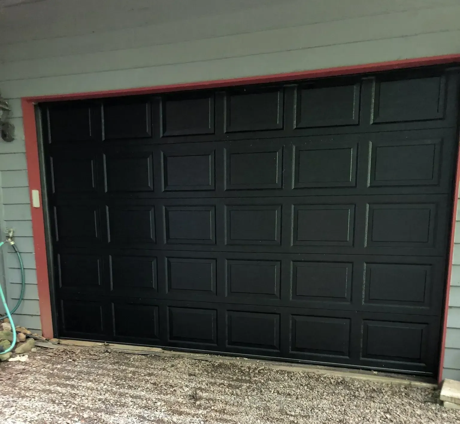 Black paneled garage door set in a light gray exterior wall with gravel in front.