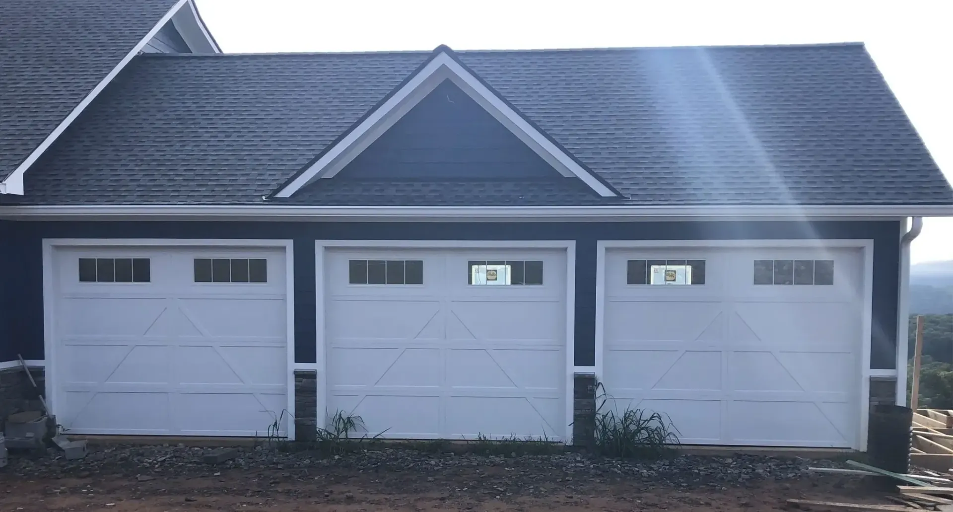Three-car garage with white doors and dark shingled roof in daylight