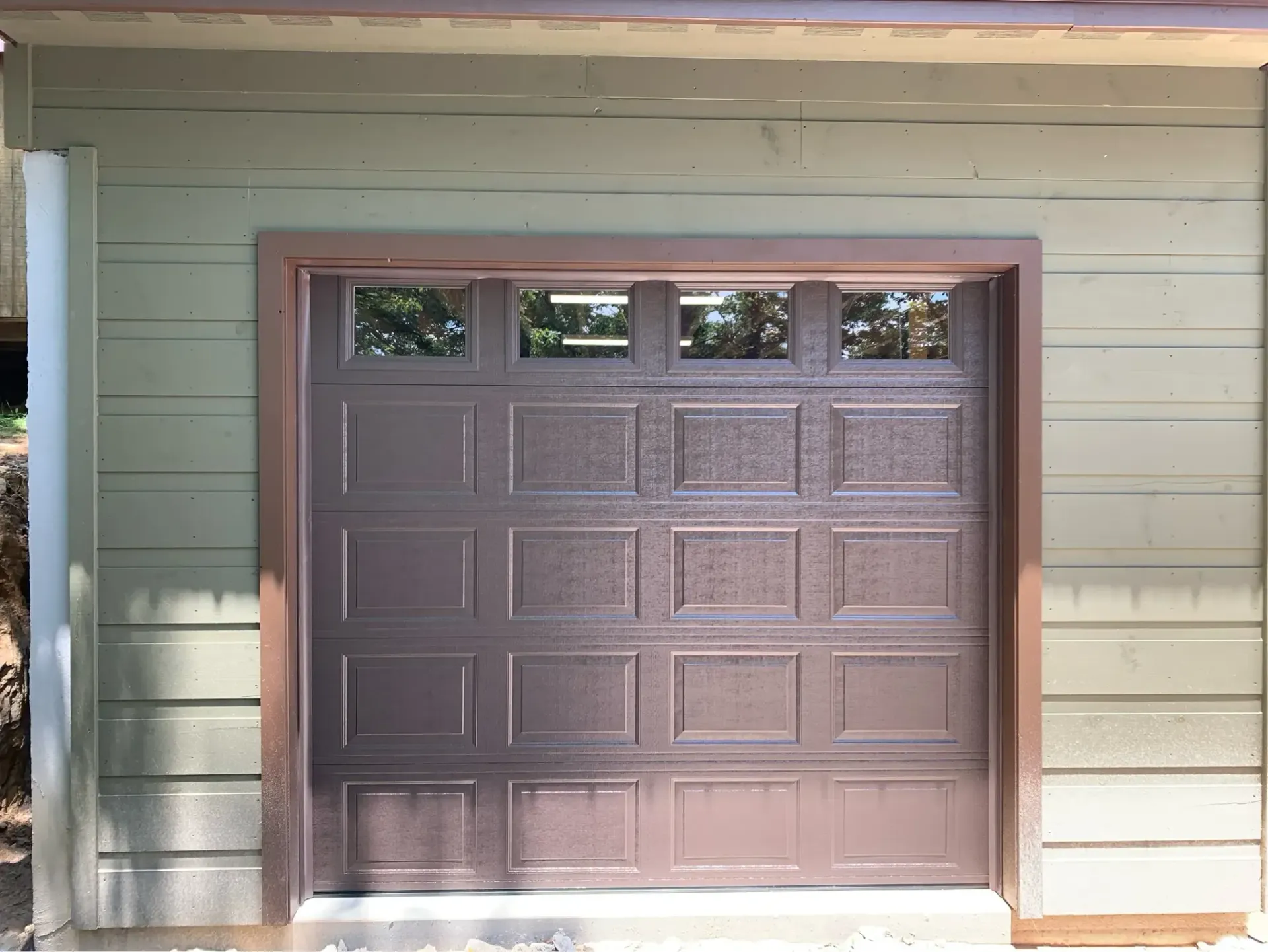 Closed brown garage door with four small windows, set in a light-colored exterior wall.