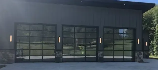 Modern building facade with three large glass garage doors and wall lights at dusk