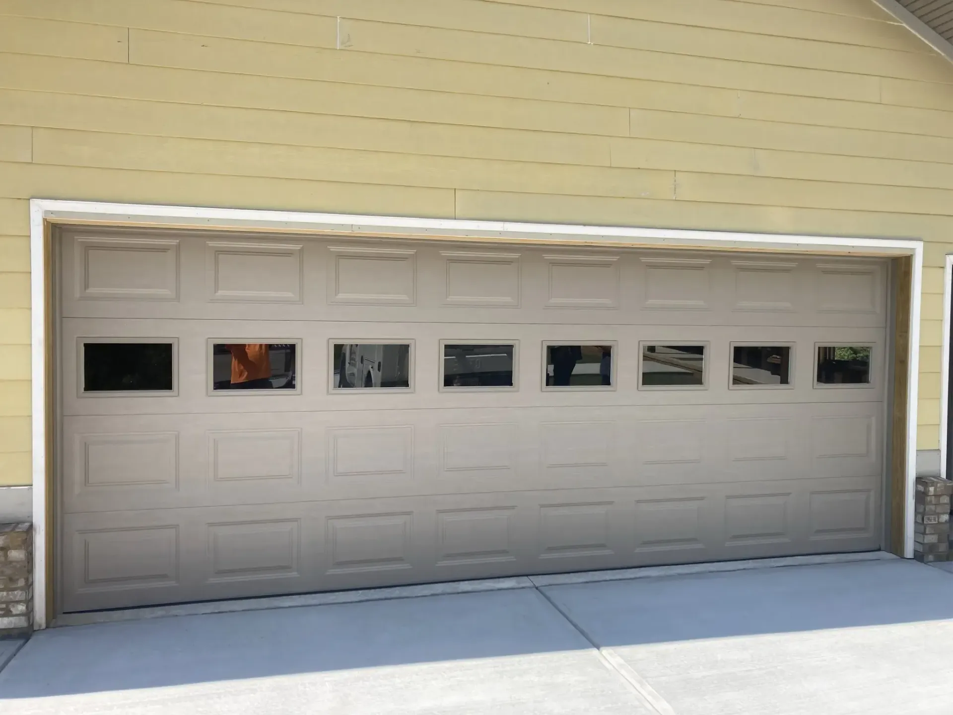 Closed beige garage door with small windows on a yellow house exterior