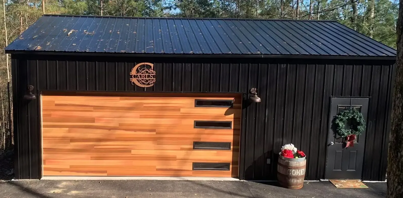 Black barn with a large wooden garage door and holiday wreath by the entrance