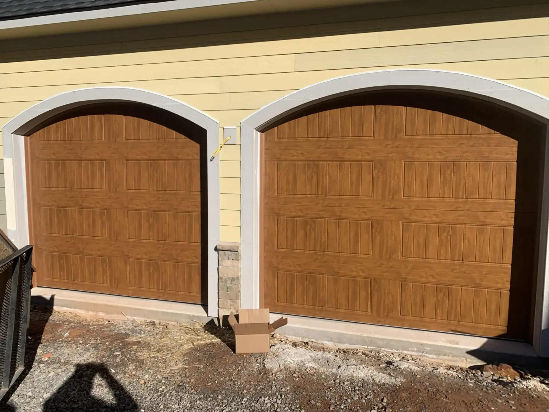 Two wooden garage doors with white trim on a beige house exterior