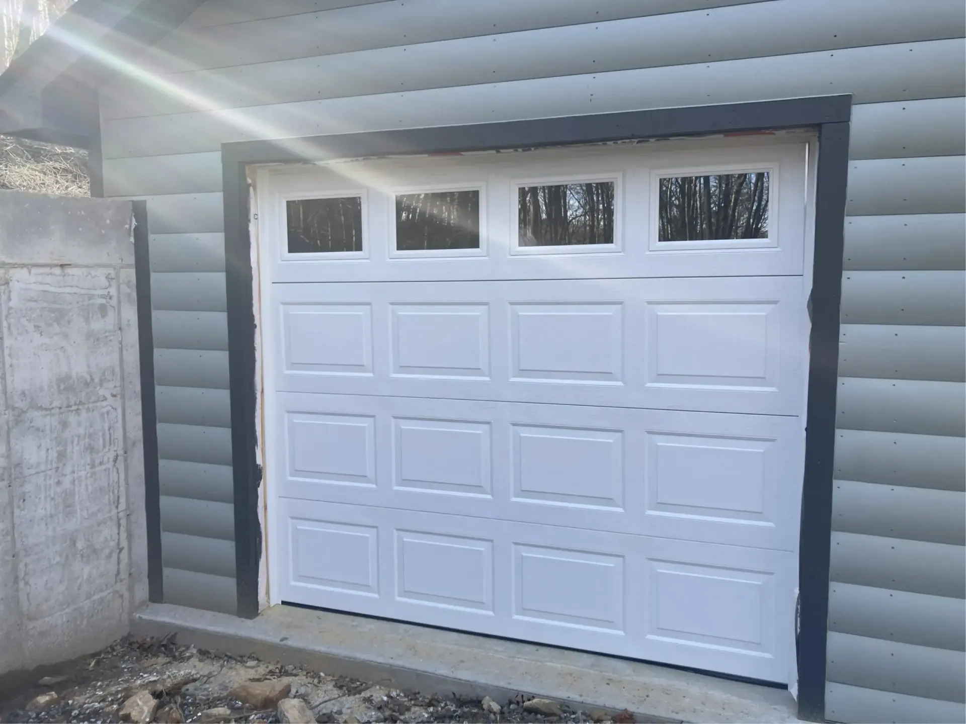 White garage door with four upper windows in a gray siding exterior wall.