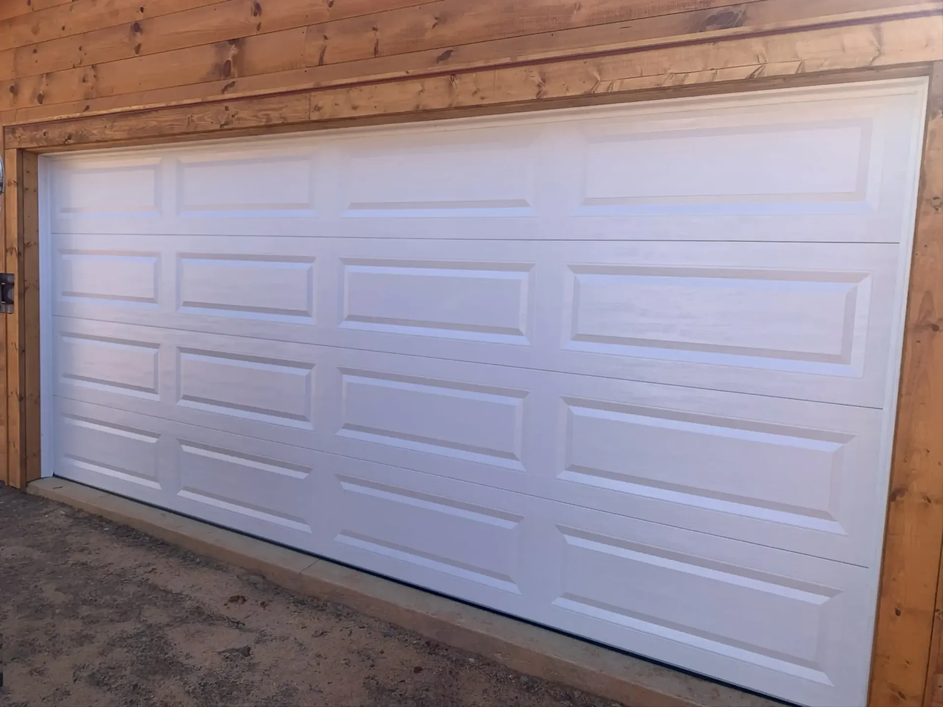 White paneled garage door in a brick driveway against a tan stucco wall.