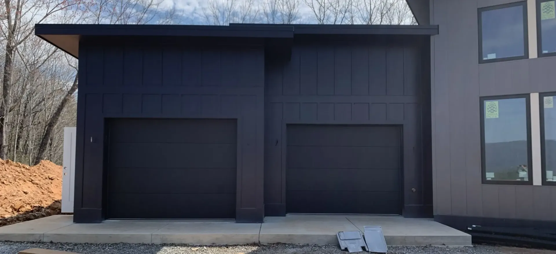 Modern house exterior with two dark garage doors and a small driveway area