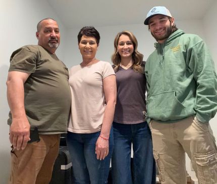 Four people standing indoors, smiling at the camera in casual clothes.