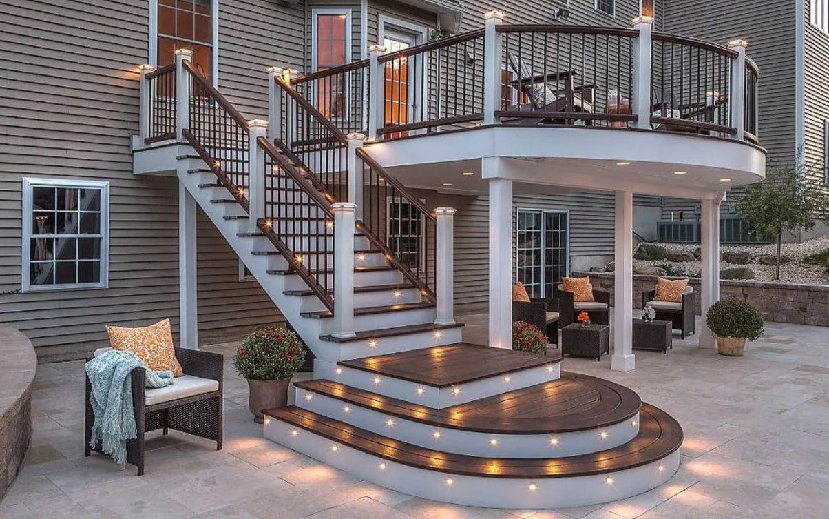 A deck with stairs leading up to it and a house in the background.