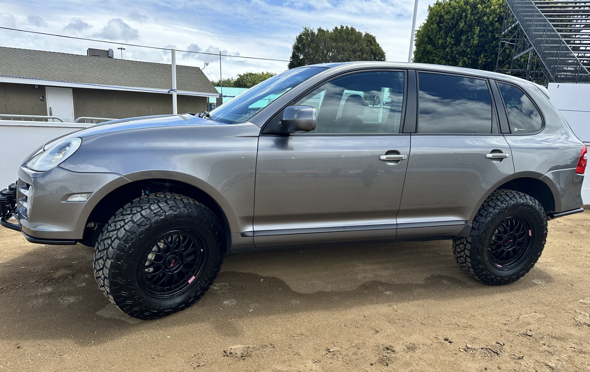 A gray off-road Porsche Cayenne is parked on a dirt road.