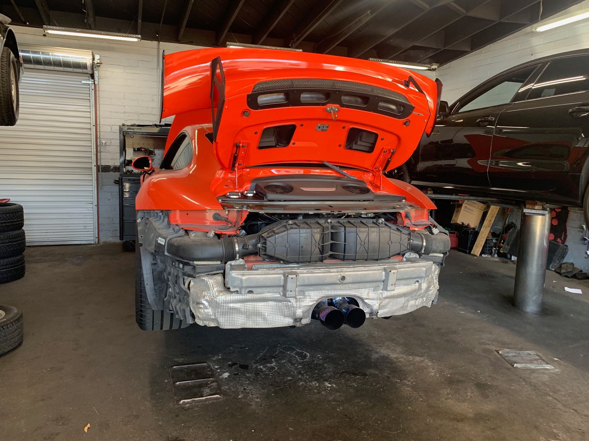 A red car with the hood up is sitting in a garage.