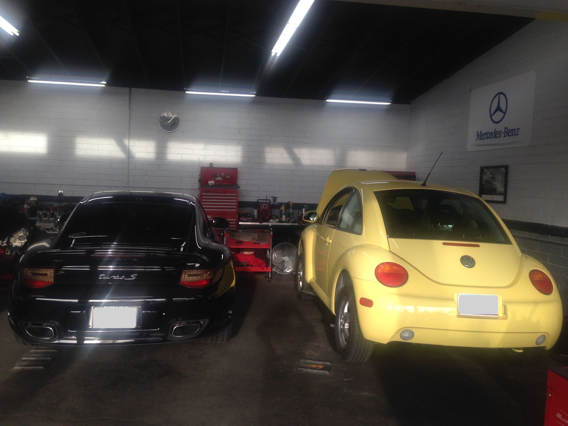 A yellow Beetle is parked next to a black car in a garage.