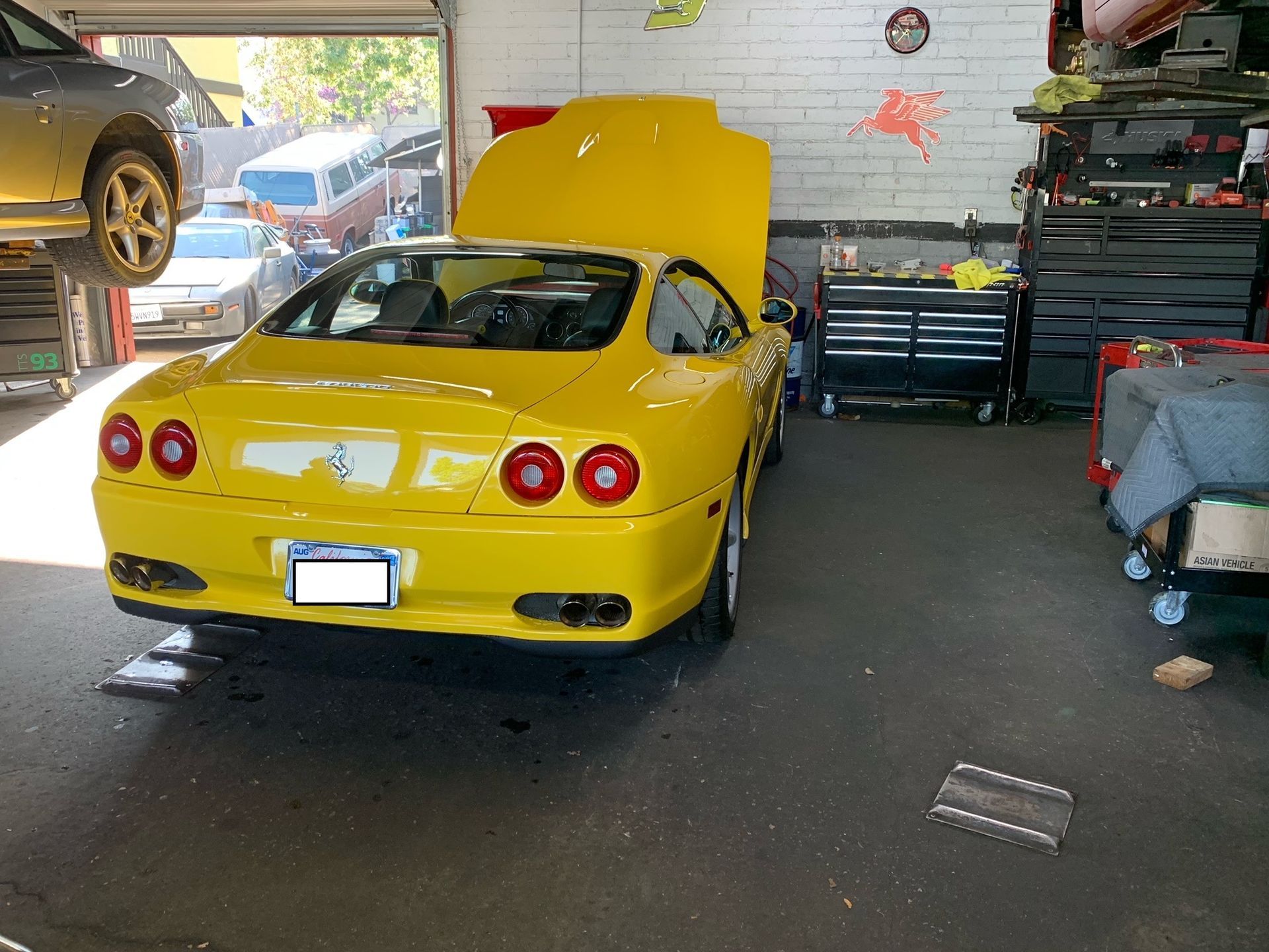 A yellow sports car with the hood up in a garage.