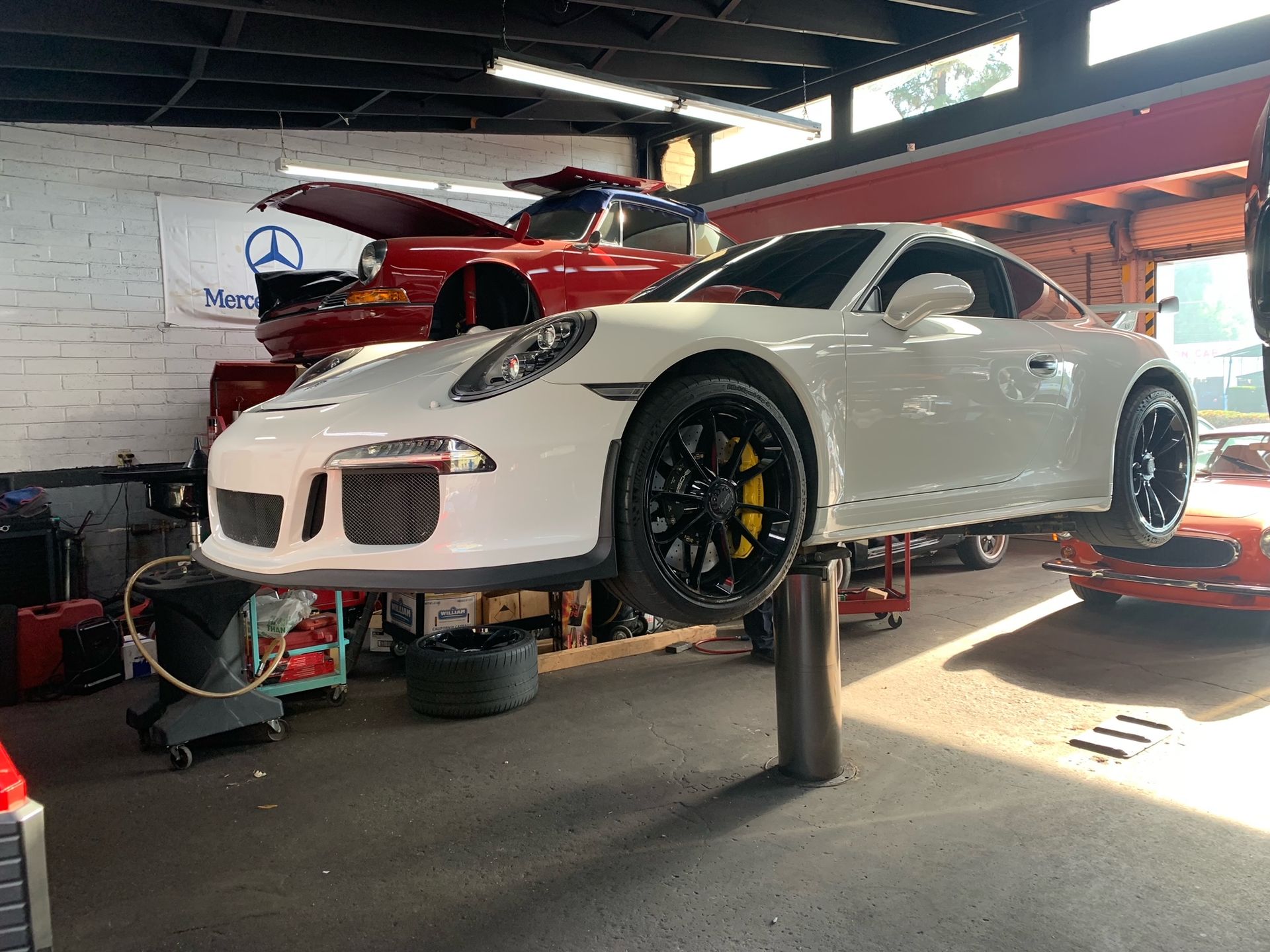 A white Porsche is sitting on a lift in a garage.