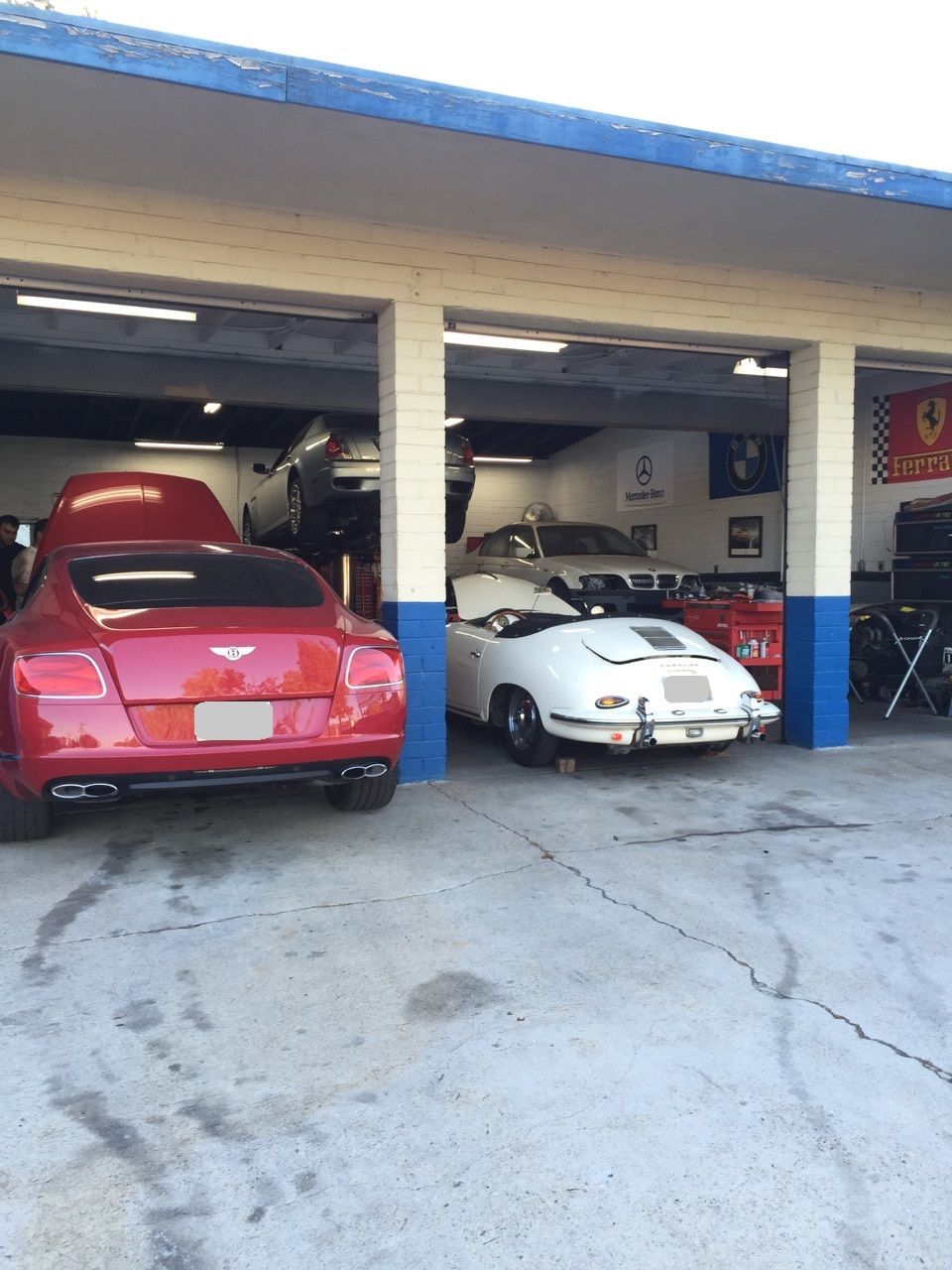 A red Bentley and a white Porsche are parked in a garage.