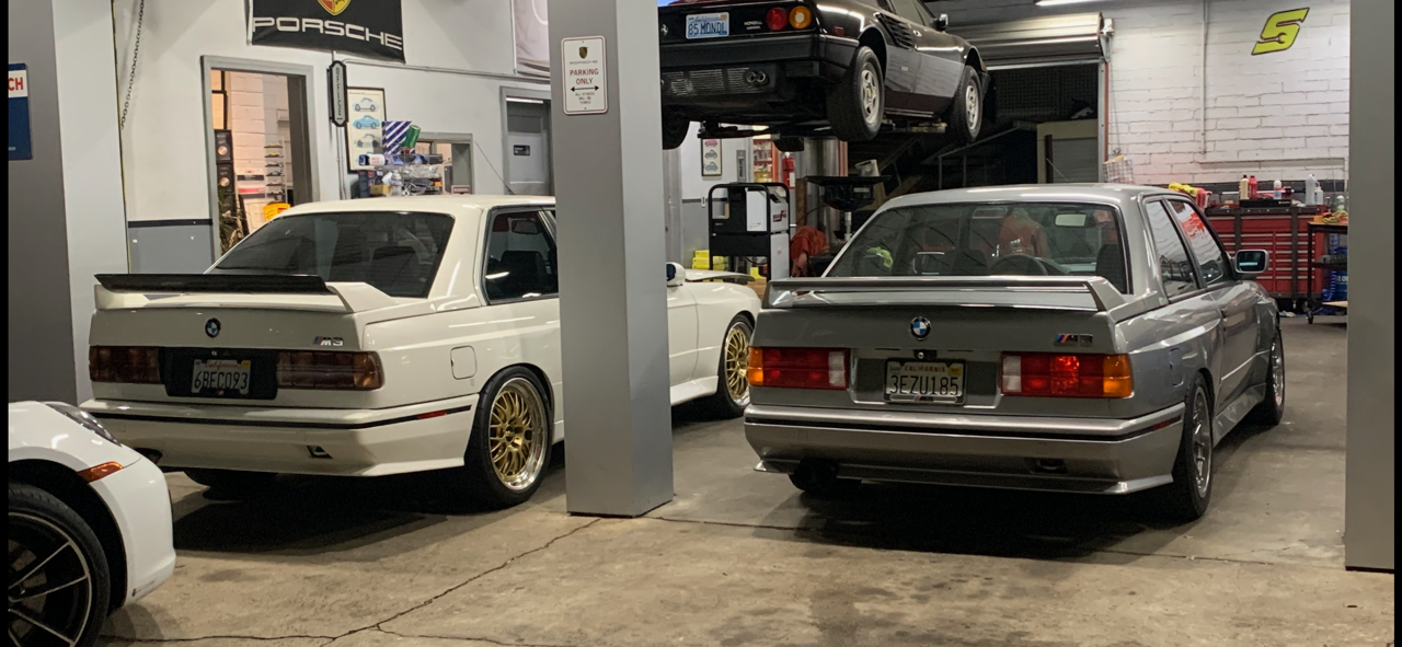 Two cars are parked in a garage next to each other.