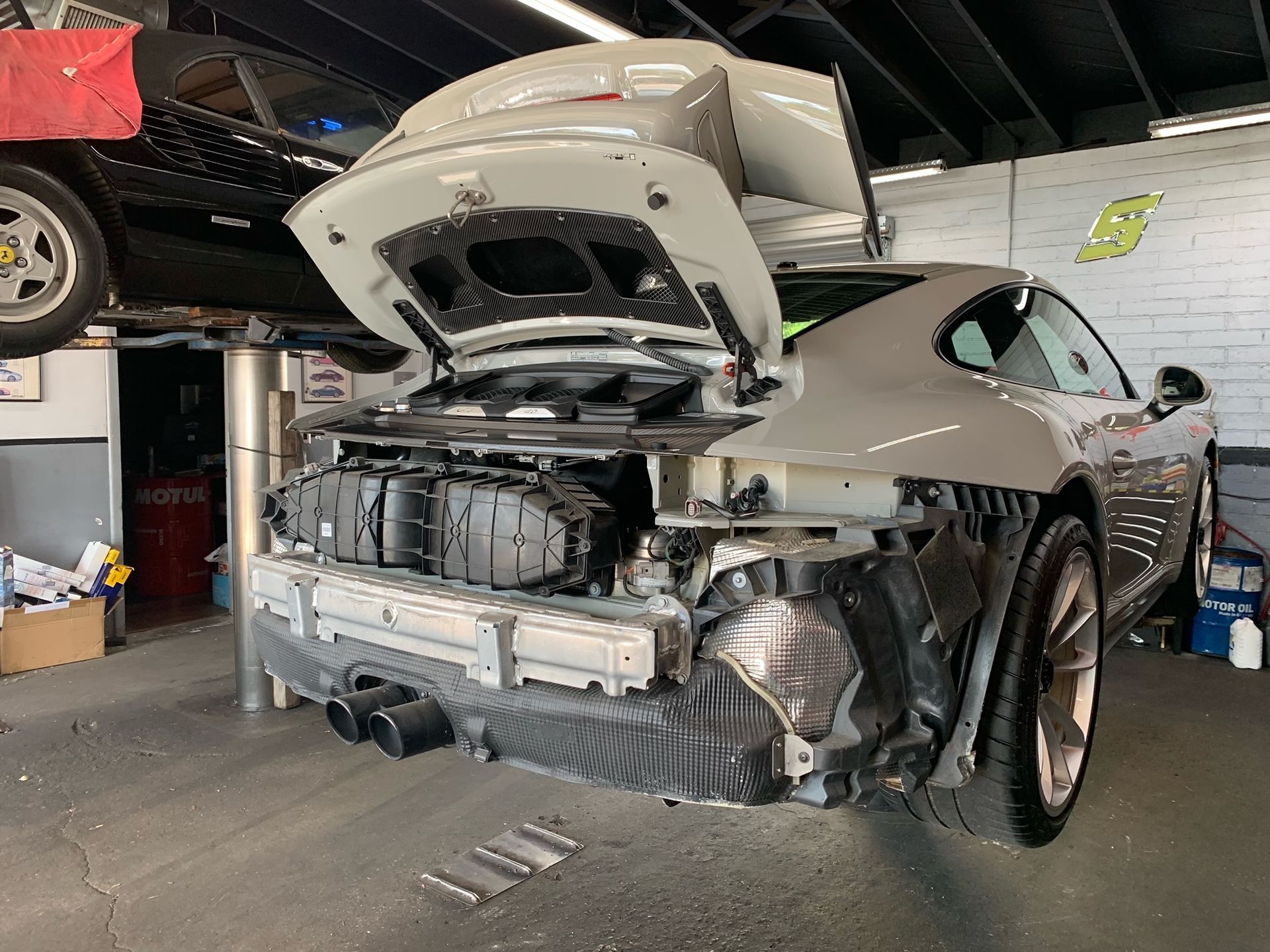 A car is being repaired in a garage with the hood open.