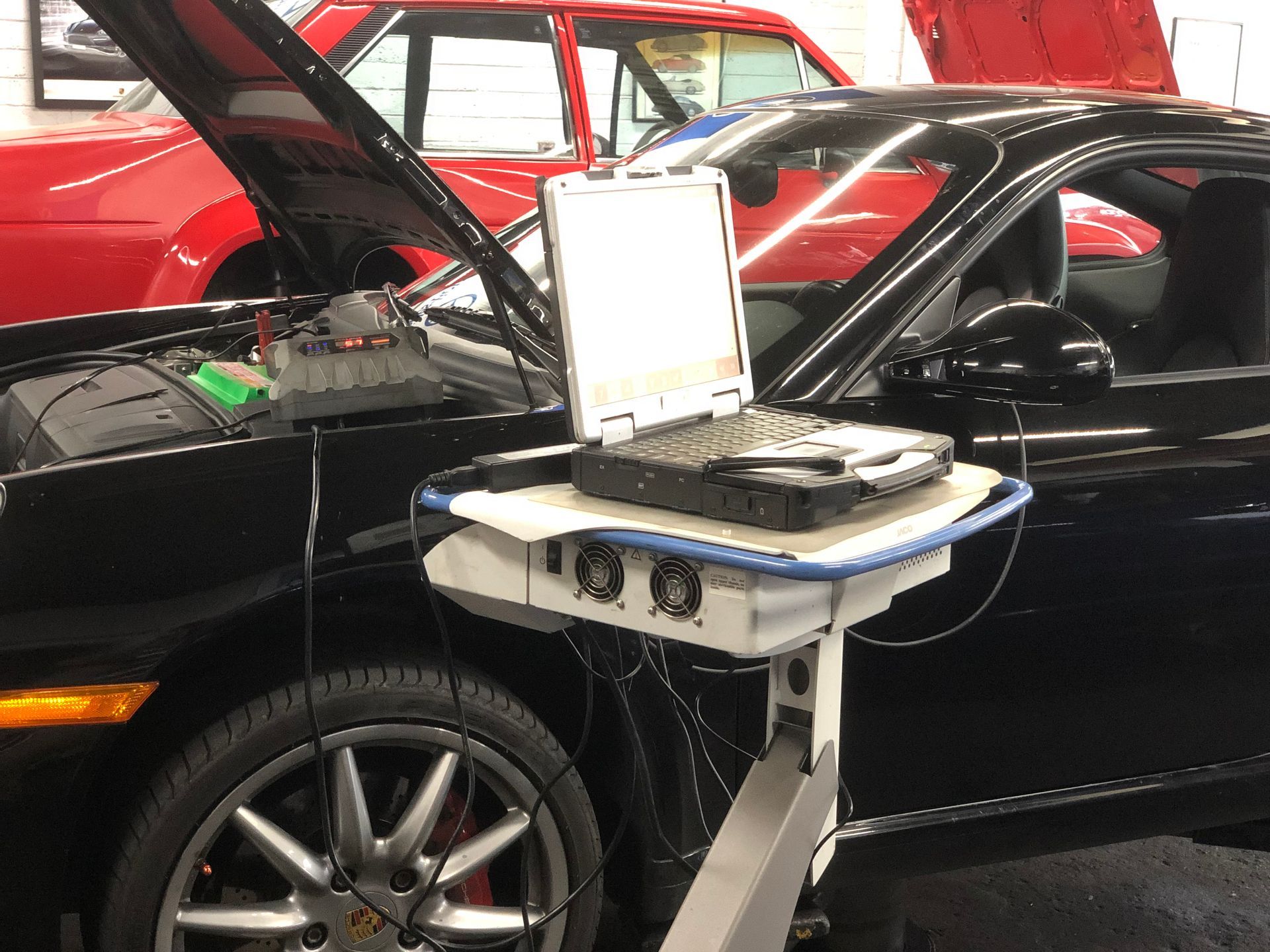 A black car with the hood open and a laptop on a cart.