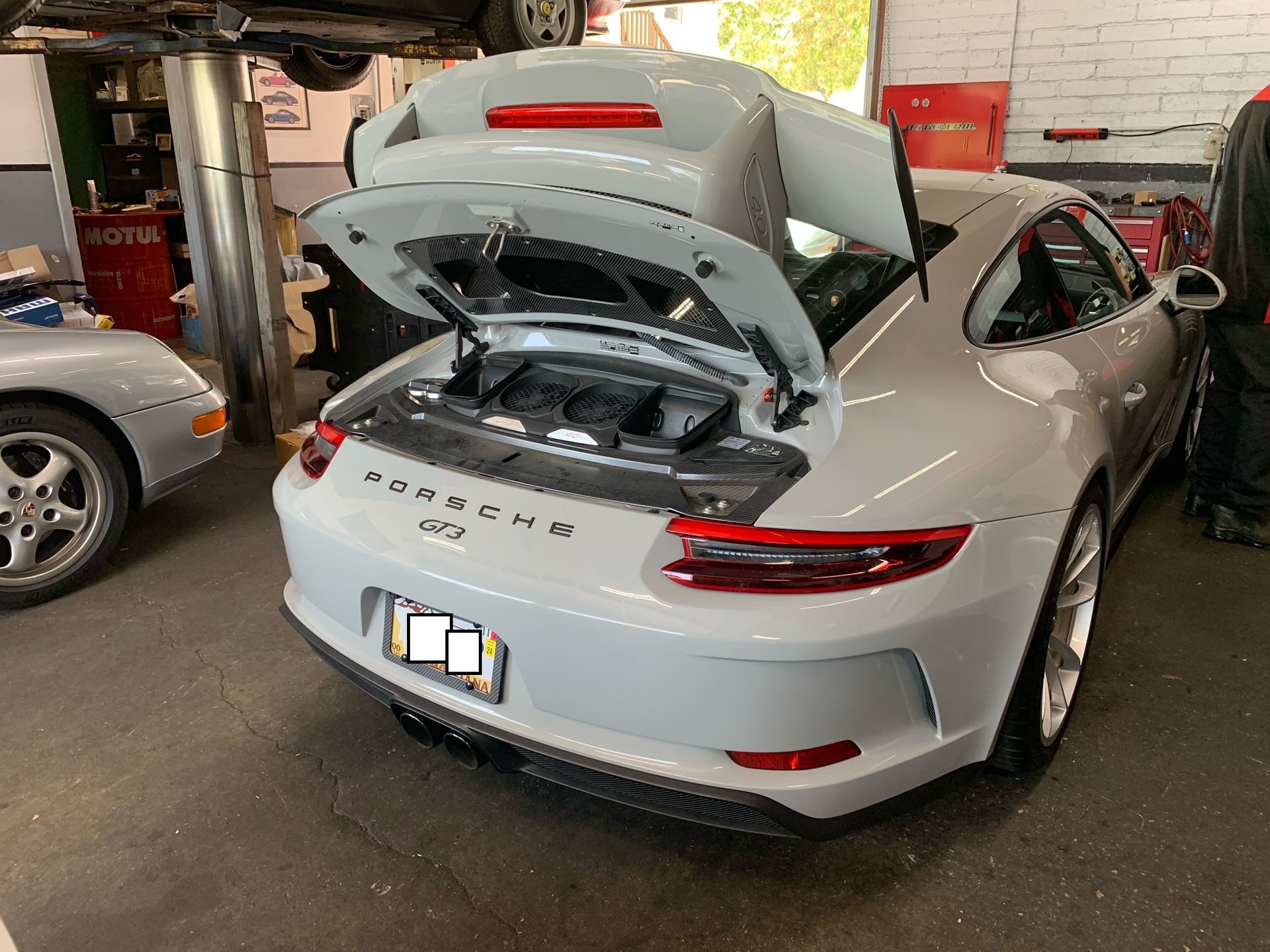 A white Porsche 911 is parked in a garage with the hood open.