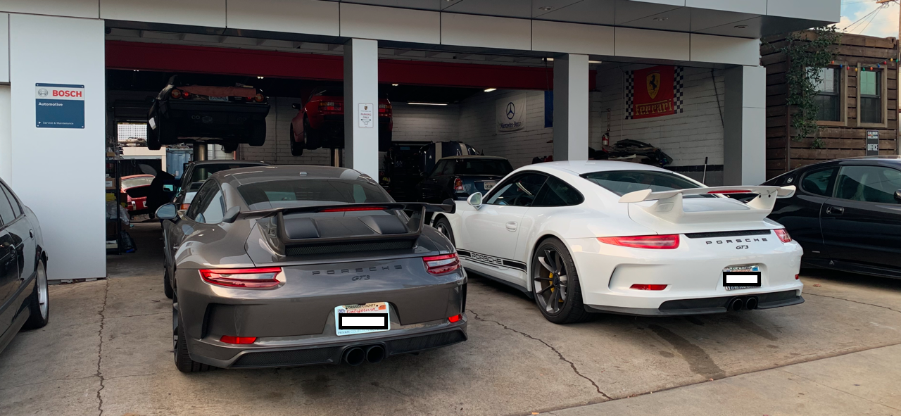 Two Porsche cars are parked in front of a garage.