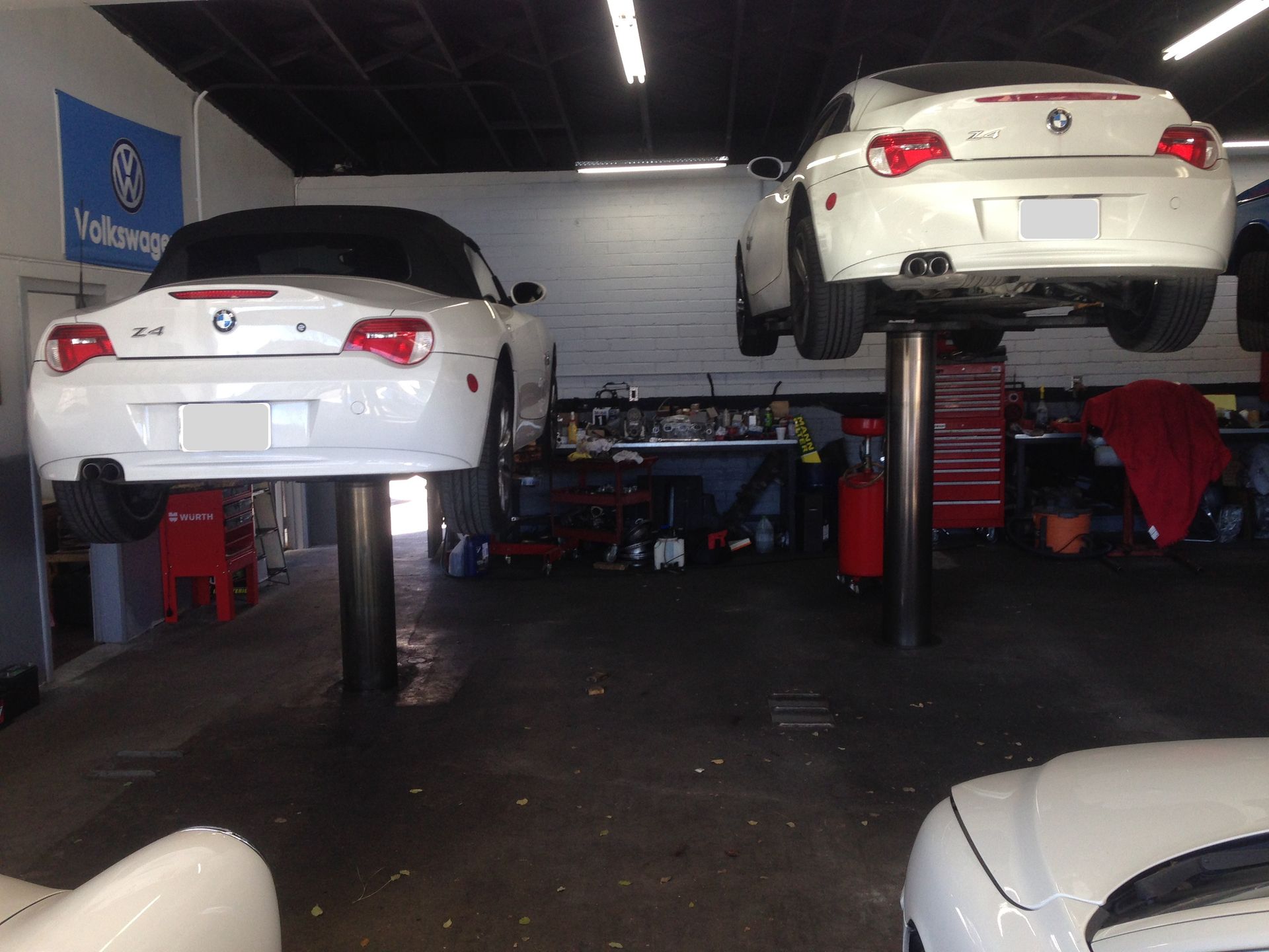 Two white cars are sitting on a lift in a garage.