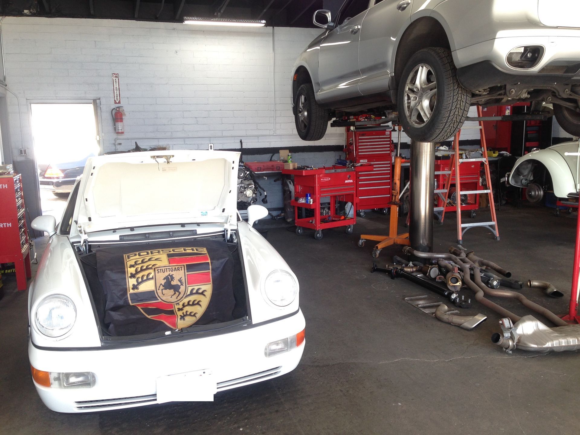 A white Porsche is sitting on a lift in a garage.