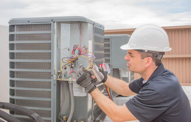 Technician in hard hat inspecting wiring on an outdoor HVAC unit