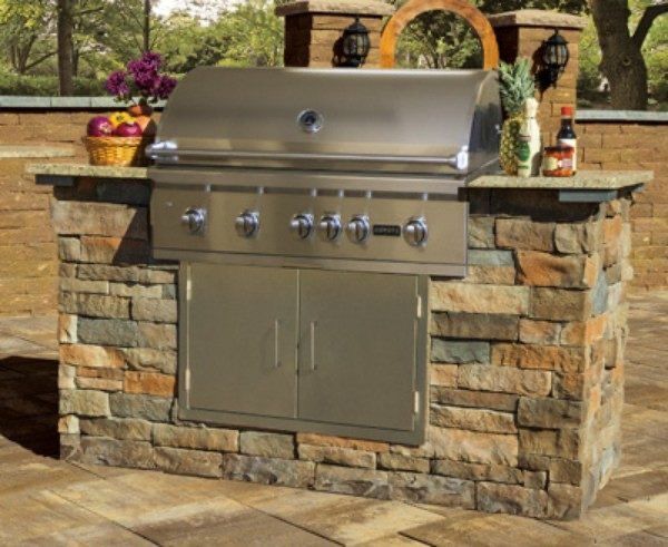 Stainless steel grill built into a stone island on a patio.