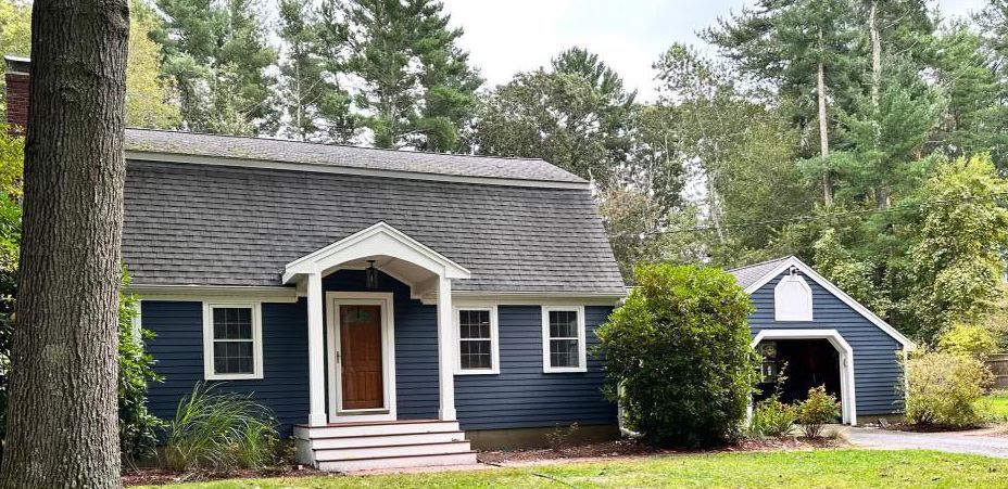 A blue house with a garage and a tree in front of it