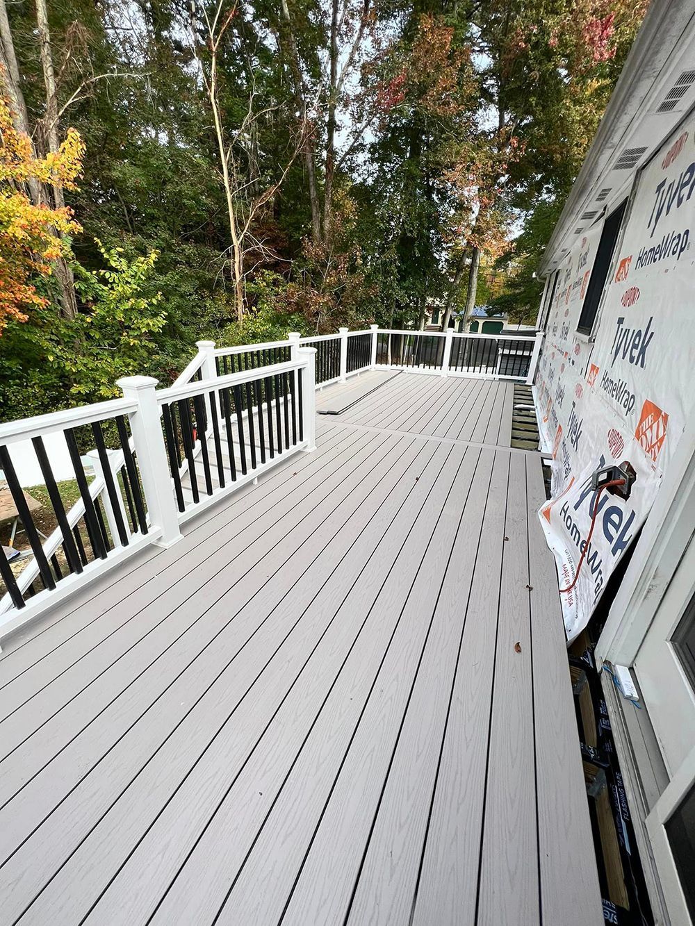 A wooden deck with a white railing and trees in the background