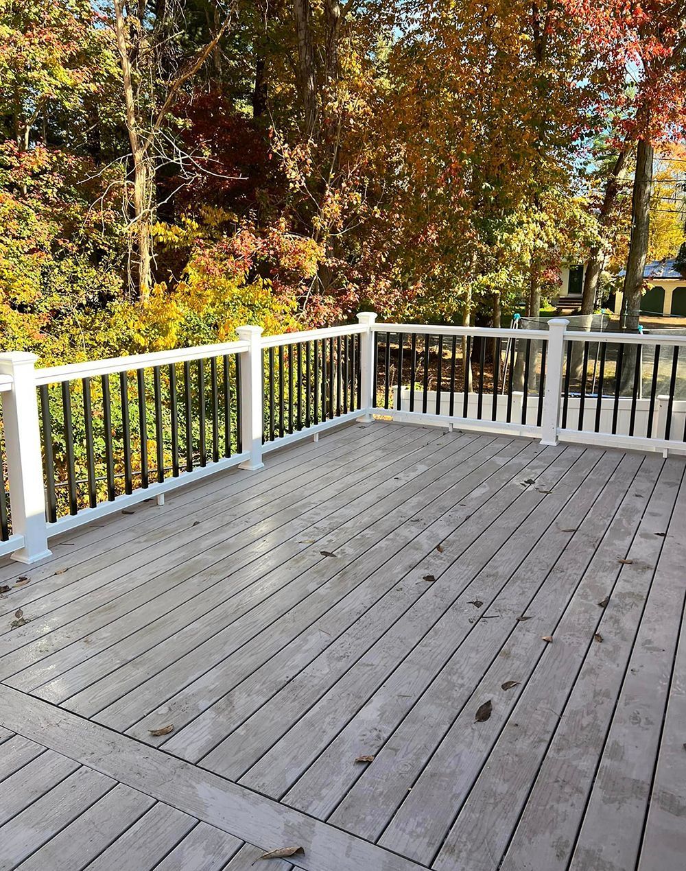 A wooden deck with a white railing and trees in the background