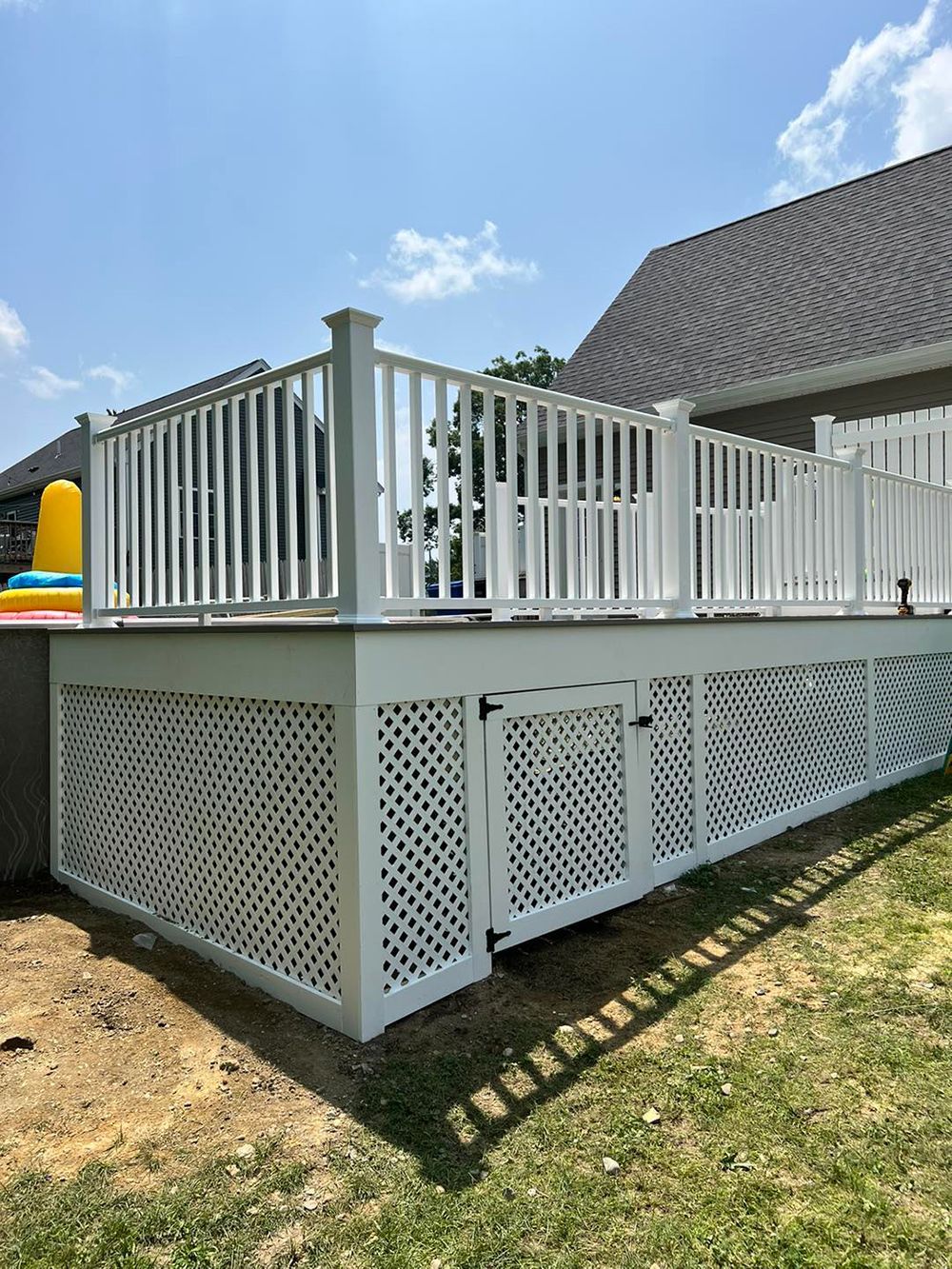 A white deck with a white railing and a fence in front of a house